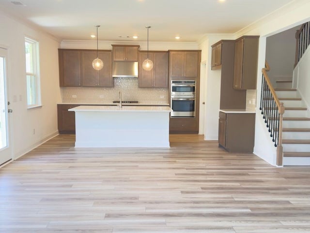 62 Sheryl Way, Loganville, GA 30052 - kitchen with under cabinet range hood, stainless steel double oven, light countertops, light wood-style floors, and tasteful backsplash