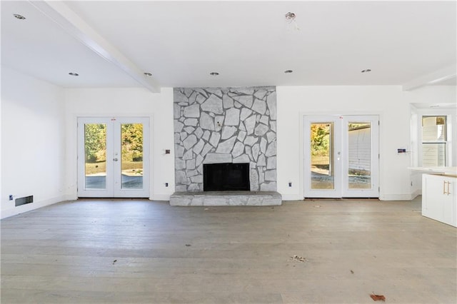 unfurnished living room featuring light hardwood / wood-style flooring, french doors, beam ceiling, and a fireplace