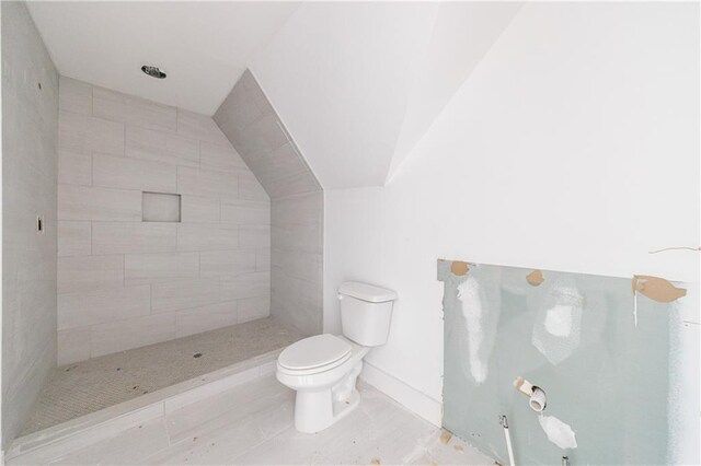 bathroom featuring a tile shower, toilet, and vaulted ceiling