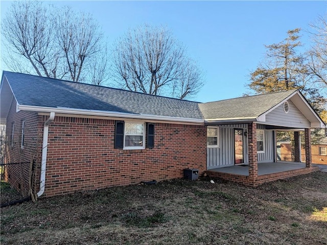 back of house with a carport, brick siding, and roof with shingles