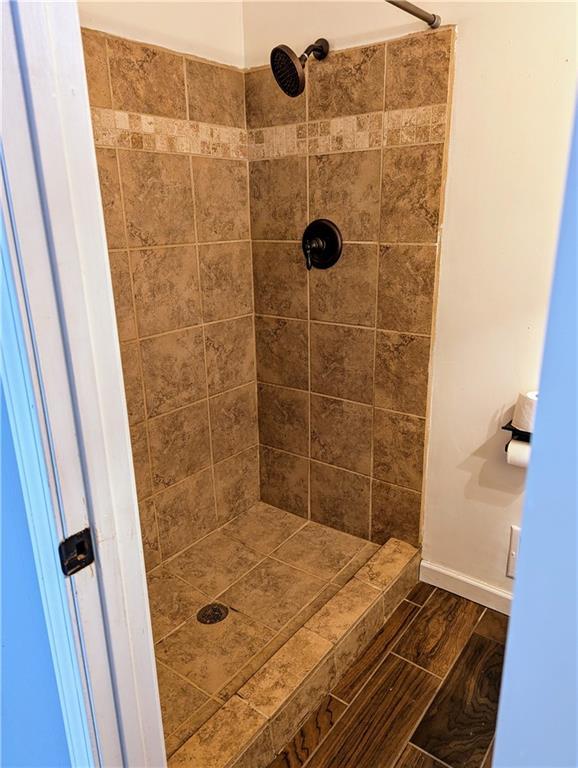 full bath with tiled shower, wood finish floors, and baseboards