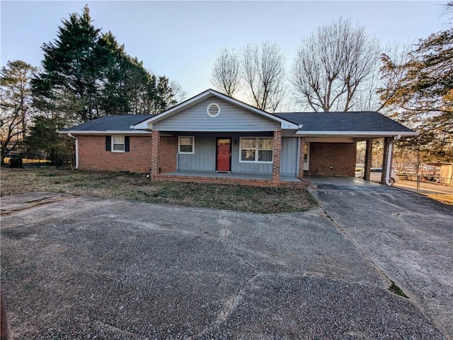 ranch-style house featuring a porch, brick siding, driveway, roof with shingles, and a carport