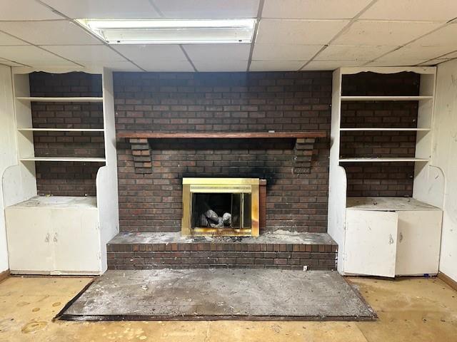 2588 Sandtown Rd SW, Marietta, GA 30060 - unfurnished living room with a brick fireplace, concrete floors, a paneled ceiling, and baseboards