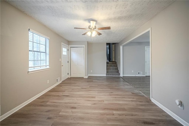 unfurnished room featuring baseboards, ceiling fan, stairway, wood finished floors, and a textured ceiling