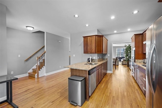 kitchen with light stone counters, sink, light hardwood / wood-style flooring, and appliances with stainless steel finishes