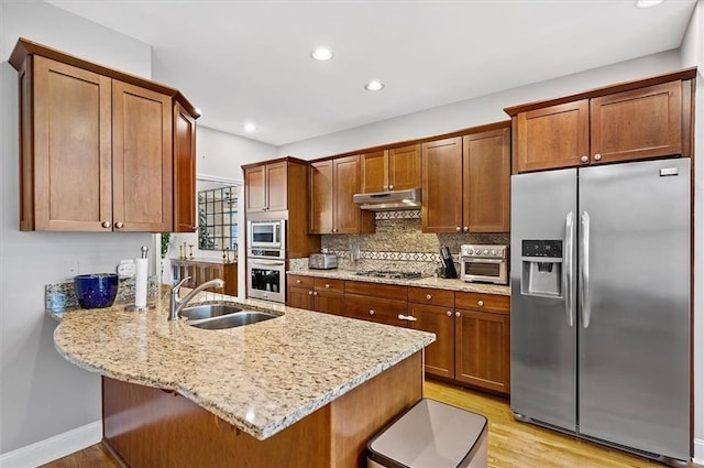 kitchen with sink, light hardwood / wood-style flooring, kitchen peninsula, a breakfast bar, and appliances with stainless steel finishes