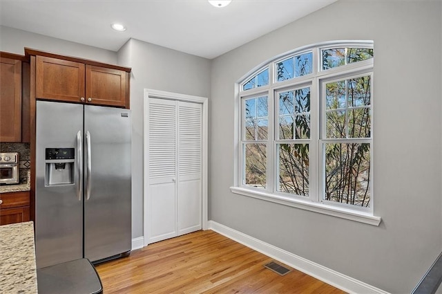 kitchen featuring light stone countertops, stainless steel fridge, light hardwood / wood-style flooring, and a healthy amount of sunlight