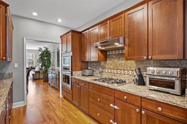 kitchen featuring tasteful backsplash, light stone counters, stainless steel appliances, and light wood-type flooring