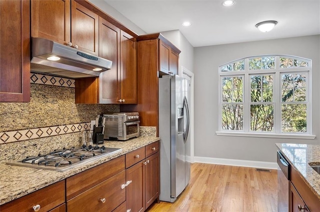 kitchen with stainless steel appliances, light stone counters, tasteful backsplash, and light hardwood / wood-style floors