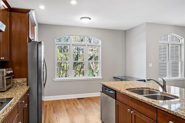 kitchen featuring appliances with stainless steel finishes, light wood-type flooring, light stone counters, and sink