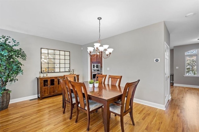 dining area with light wood-type flooring and an inviting chandelier