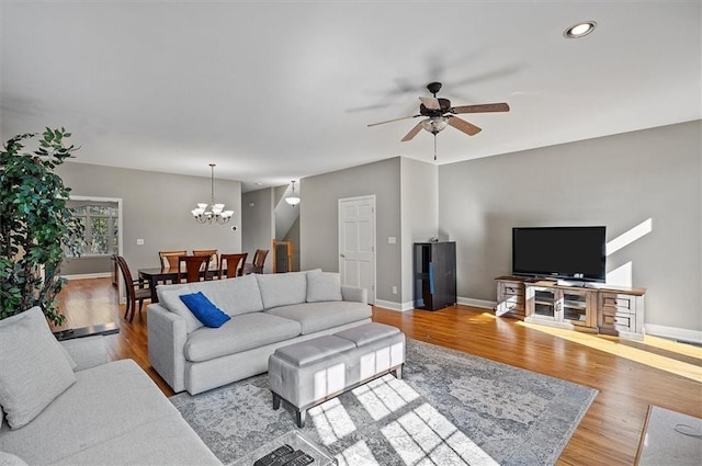 living room with ceiling fan with notable chandelier and light hardwood / wood-style flooring