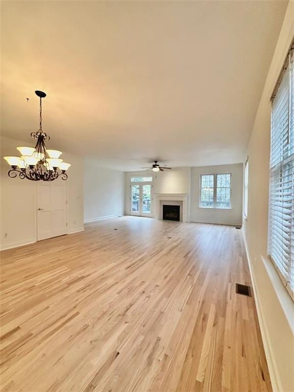 unfurnished living room featuring ceiling fan with notable chandelier, light wood-type flooring, and a healthy amount of sunlight