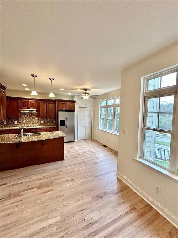 kitchen featuring a wealth of natural light, stainless steel fridge, decorative light fixtures, and light wood-type flooring