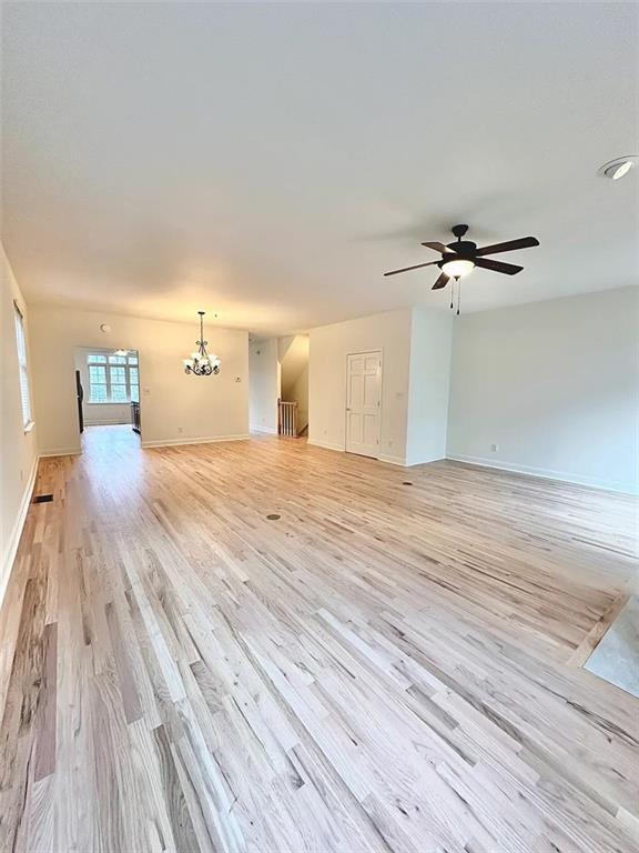 unfurnished living room with ceiling fan with notable chandelier and light wood-type flooring