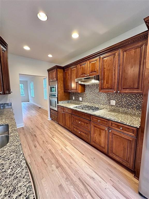 kitchen featuring appliances with stainless steel finishes, light wood-type flooring, light stone counters, and sink