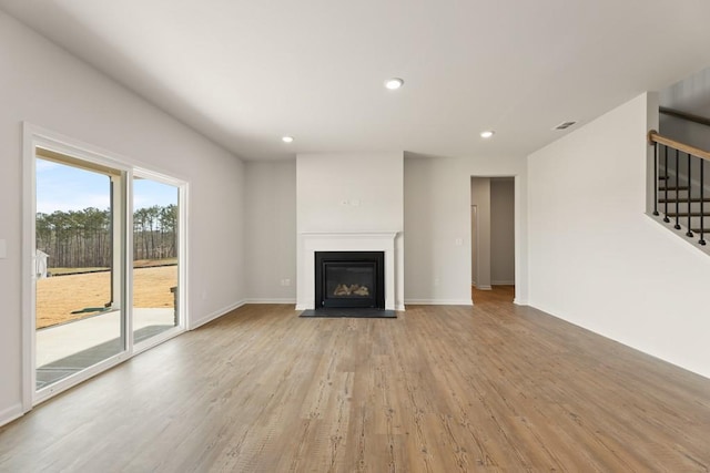 unfurnished living room featuring recessed lighting, light wood-style flooring, stairs, and a glass covered fireplace