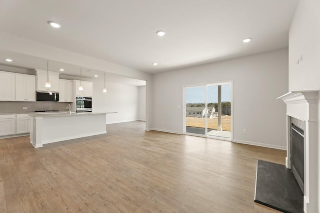 unfurnished living room with recessed lighting, light wood-style flooring, a fireplace with flush hearth, a sink, and baseboards