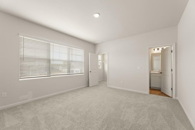 unfurnished bedroom featuring a spacious closet, baseboards, connected bathroom, and light colored carpet