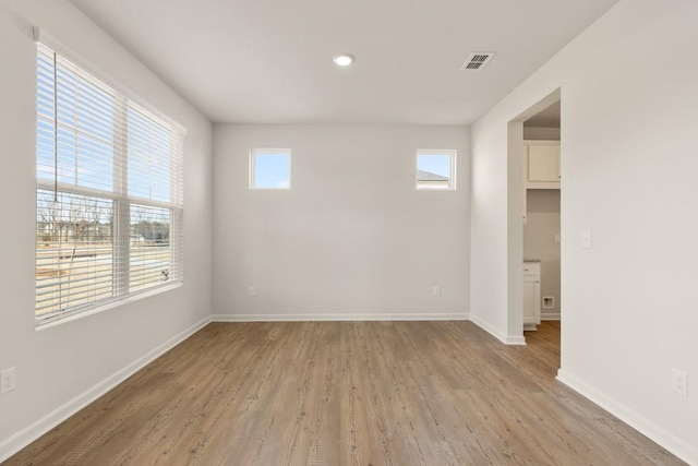 empty room featuring a healthy amount of sunlight, light wood-type flooring, visible vents, and baseboards