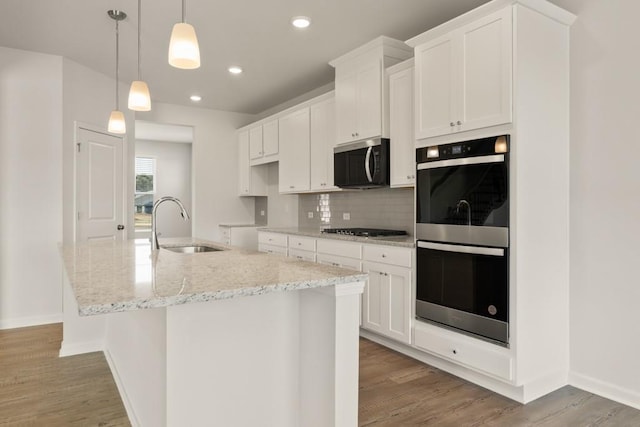 kitchen featuring a sink, light wood-style floors, appliances with stainless steel finishes, tasteful backsplash, and an island with sink