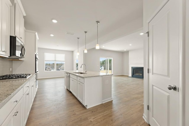 kitchen with light wood finished floors, white cabinets, appliances with stainless steel finishes, a sink, and backsplash