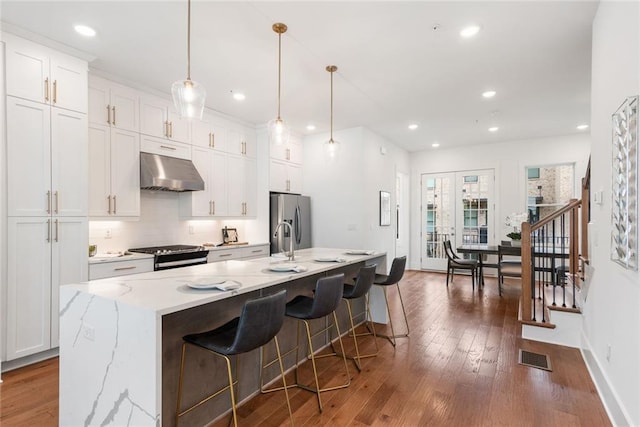 1032 Robert Smalls Way, Atlanta, GA 30318 - kitchen featuring under cabinet range hood, appliances with stainless steel finishes, hardwood / wood-style flooring, a center island with sink, and white cabinets