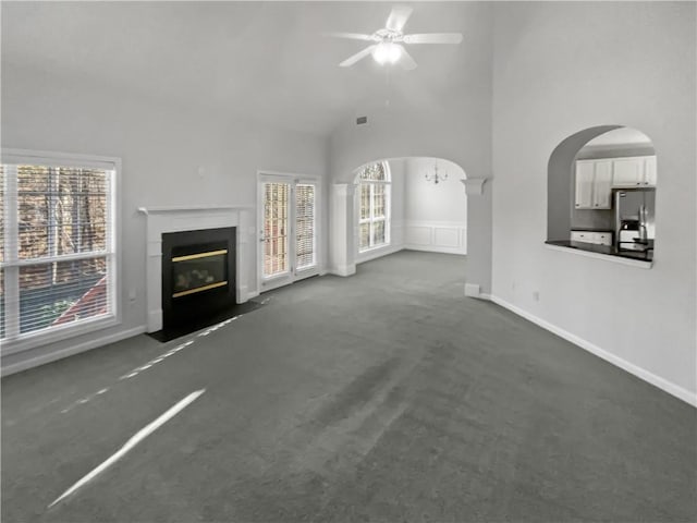 unfurnished living room with a healthy amount of sunlight, a towering ceiling, arched walkways, and dark carpet