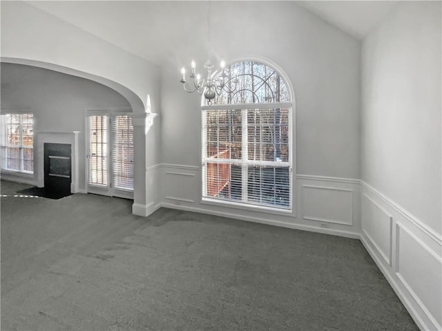 unfurnished dining area with a wainscoted wall, carpet, a fireplace with flush hearth, and an inviting chandelier