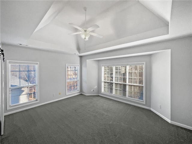 empty room with baseboards, a raised ceiling, a ceiling fan, and dark colored carpet