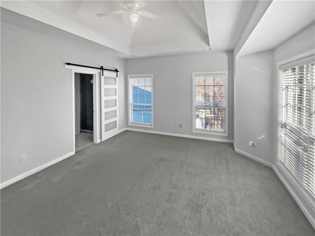 carpeted spare room with ceiling fan, a tray ceiling, a barn door, and baseboards