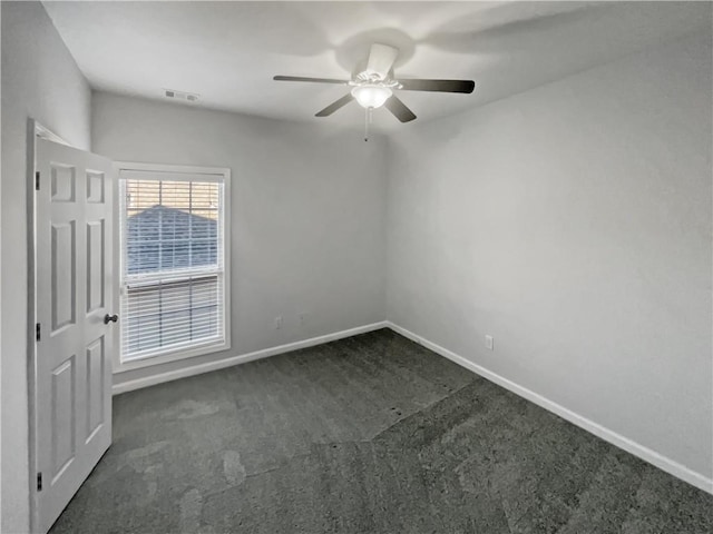 empty room with ceiling fan, dark carpet, visible vents, and baseboards