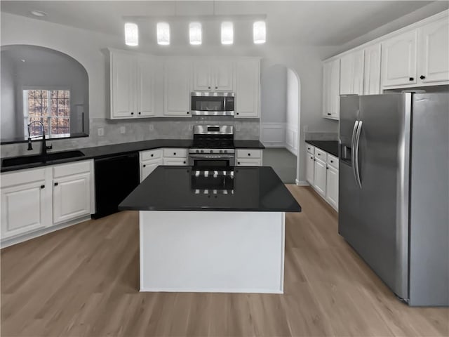 kitchen with arched walkways, white cabinets, dark countertops, stainless steel appliances, and a sink