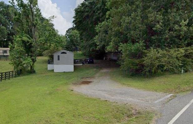 view of yard with driveway, a storage unit, and fence