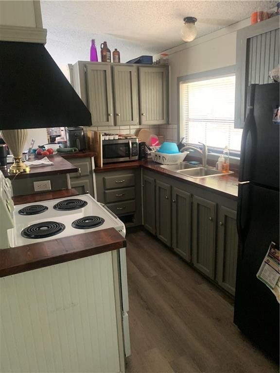 kitchen with dark countertops, stainless steel microwave, freestanding refrigerator, ventilation hood, and a sink