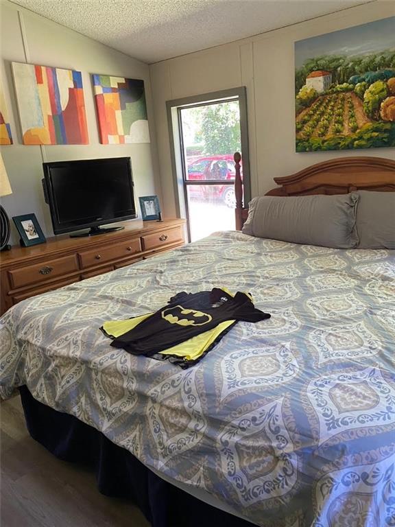 bedroom with vaulted ceiling, a textured ceiling, and wood finished floors