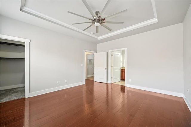 unfurnished bedroom featuring a raised ceiling, baseboards, and wood finished floors