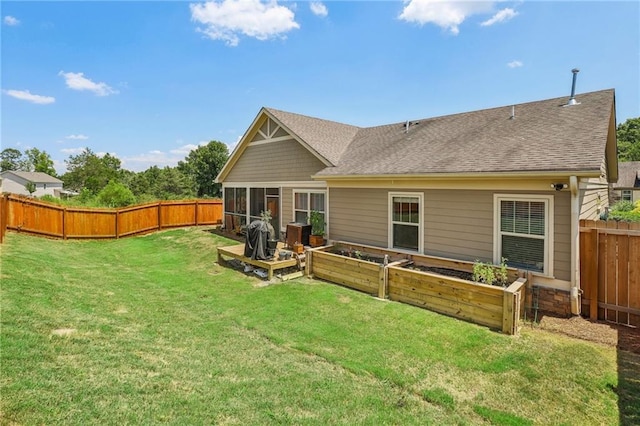 back of property with a shingled roof, a fenced backyard, a sunroom, a yard, and a garden