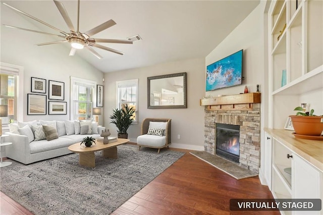 living room featuring dark wood-style floors, visible vents, lofted ceiling, ceiling fan, and a stone fireplace