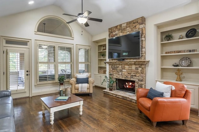 living room with a stone fireplace, ceiling fan, dark wood-type flooring, and built in shelves