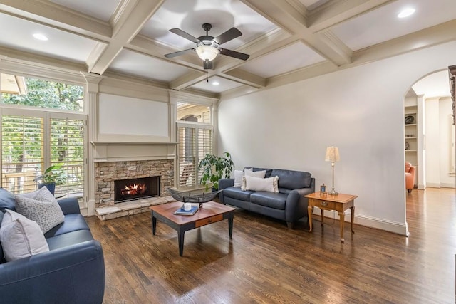 living room featuring beam ceiling, dark wood-type flooring, a stone fireplace, and ceiling fan