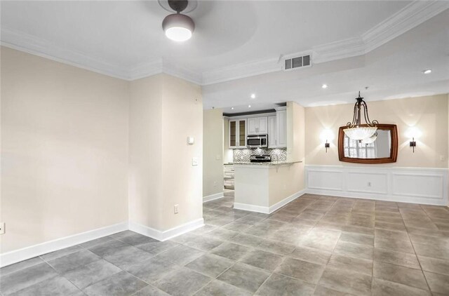 unfurnished living room with a decorative wall, visible vents, crown molding, and baseboards