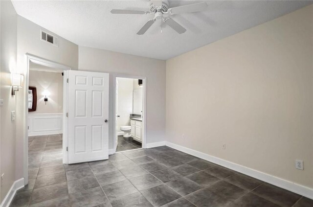 unfurnished bedroom featuring dark tile patterned floors, connected bathroom, visible vents, and ceiling fan