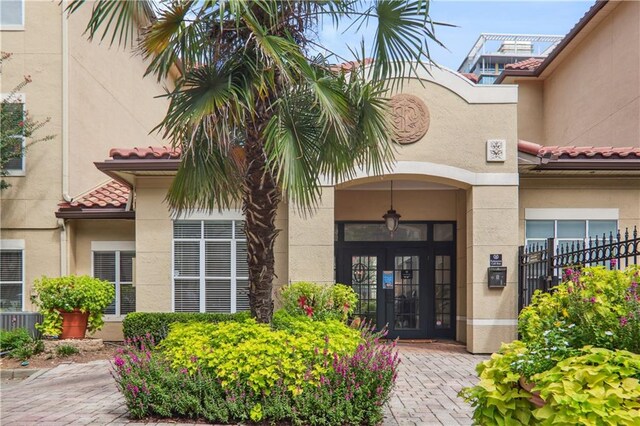 view of exterior entry featuring a tile roof, central AC unit, fence, and stucco siding
