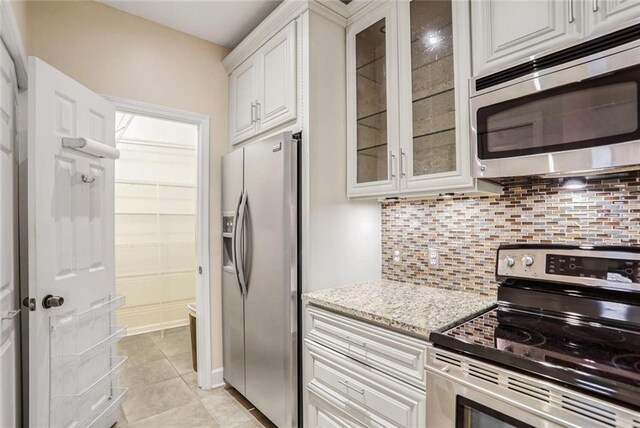 kitchen featuring light stone counters, glass insert cabinets, white cabinetry, appliances with stainless steel finishes, and decorative backsplash