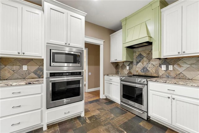 kitchen with light stone counters, white cabinetry, stainless steel appliances, custom range hood, and decorative backsplash