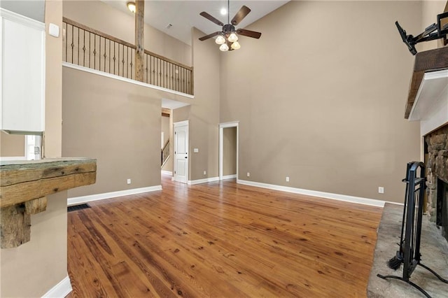 unfurnished living room featuring ceiling fan, hardwood / wood-style flooring, a fireplace, and a high ceiling