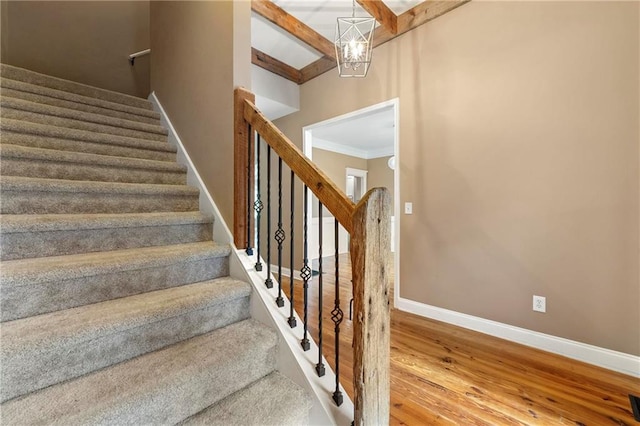 stairway with a notable chandelier, hardwood / wood-style flooring, and beam ceiling