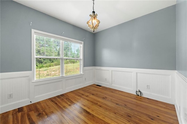 unfurnished room featuring an inviting chandelier, wood-type flooring, and a healthy amount of sunlight