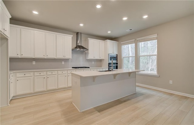 251 Arnewood Cir, Mcdonough, GA 30253 - kitchen featuring wall chimney range hood, light countertops, stovetop, light wood-style flooring, and recessed lighting